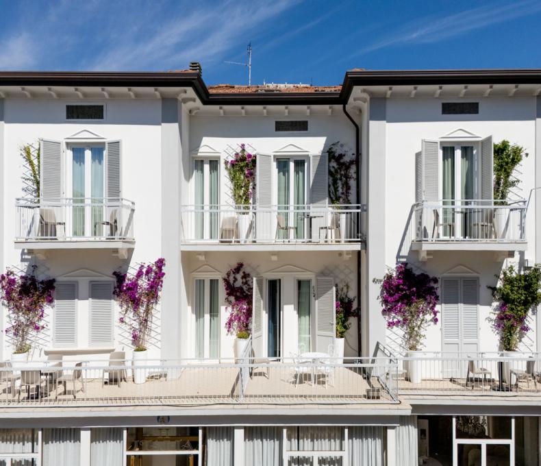 White building with balconies and flowering plants, blue sky in the background.