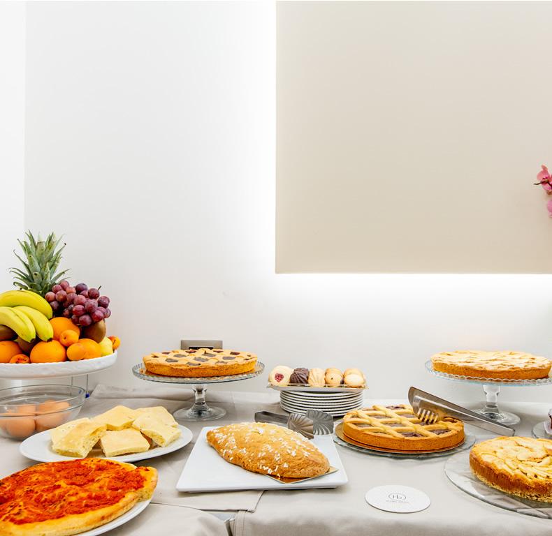 Buffet con frutta fresca, dolci e focaccia in un ambiente luminoso.