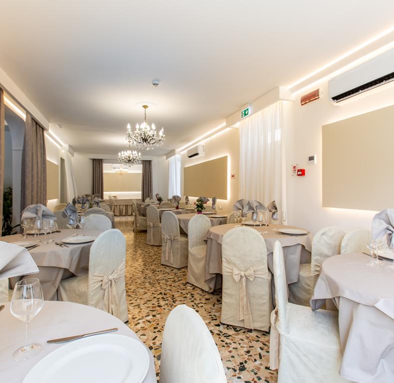 Elegante sala da pranzo con tavoli apparecchiati e lampadari decorativi.