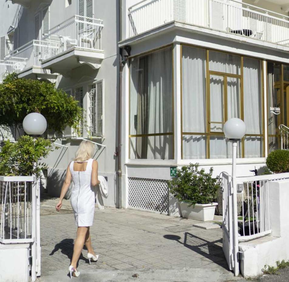 Woman in white dress entering a white building with balconies.