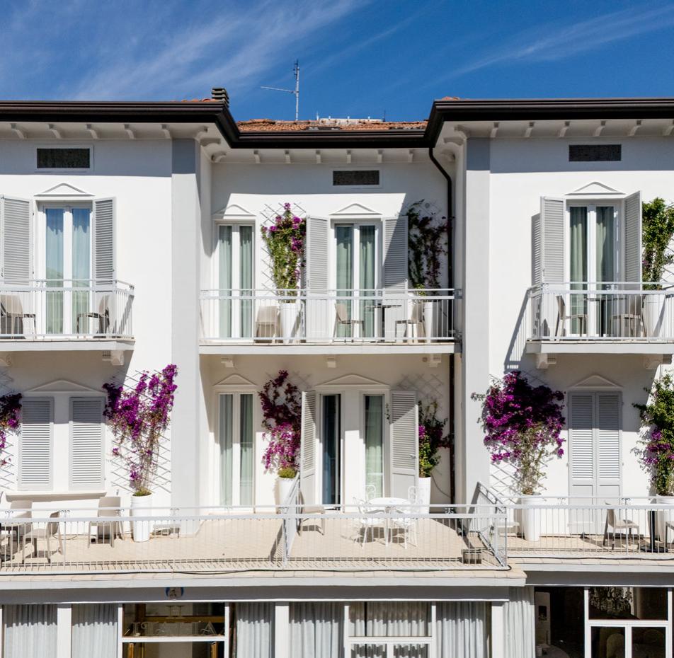 White building with balconies and flowering plants, blue sky in the background.